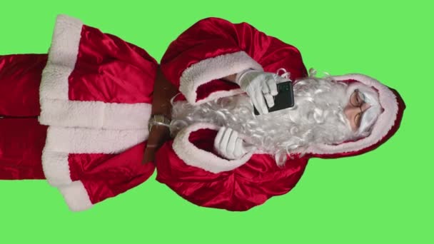 垂直视频父亲圣诞节前视图在智能手机上寻找礼物的想法 使用在线浏览器传播圣诞节的积极因素 Santa Claus穿着西服 在绿屏背景下拿着移动吸盘 — 图库视频影像