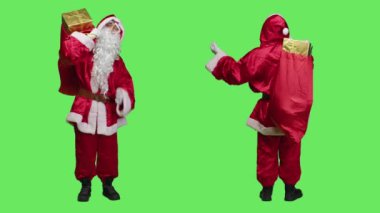 Kırmızı çantalı Noel Baba, geleneksel tatil kostümü ve gözlük takarak tüm yeşil perde arkaplanının üzerinde ho ho ho diyor. Noel Baba kostümü hediye ve oyuncaklarla dolu çanta taşıyor..