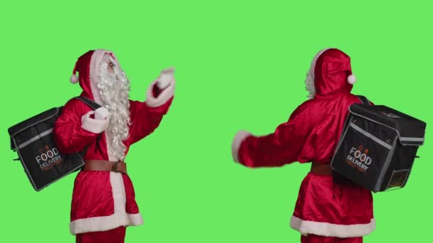 身穿桑塔西服 背包着绿色背景的送货上门的男人 穿着节日圣诞前夕的传统服装送餐 快乐的人会带来节日的气氛 — 图库视频影像