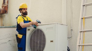 Hasarlı bileşenleri kontrol etmek için harici klima metal bobin panelini etkisiz hale getiren öncü mühendis. Hassas tamirci bozuk HVC sistemini tamir ediyor