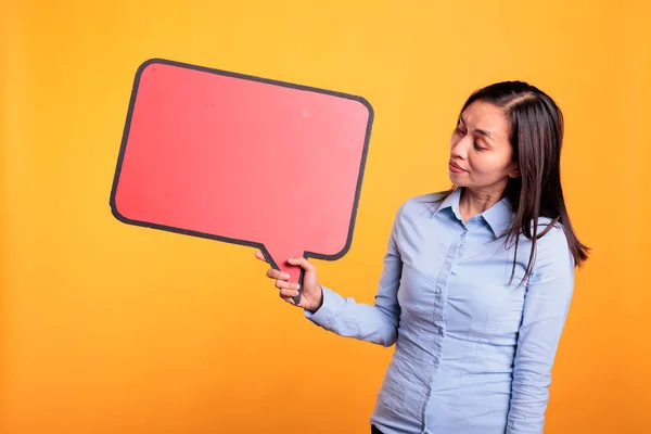 亚洲年轻人持空白的红色语音泡沫与复制空间 广告美容产品 女人站在工作室黄色的背景上 看着空白的对话框 里面有文字的位置 — 图库照片