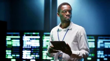 Veri merkezi güvenlik özelliklerini kontrol etmek için tablet kullanan Afrikalı Amerikalı uzman izinsiz erişim, veri ihlali, DDoS saldırıları ve diğer siber güvenlik tehditlerine karşı koruma sağlıyor.