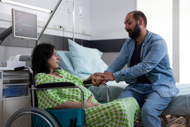 Kocası tekerlekli sandalyede oturan hamile kadını rahatlatıyor ve sezaryen ameliyatından önce ebeveynlik hakkında konuşuyor. Doğum kliniğinde bekleyen genç ebeveynler. Tıp konsepti