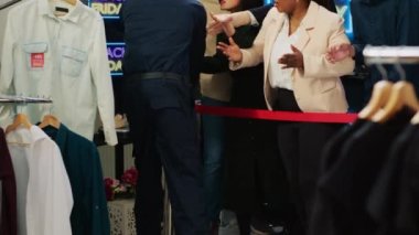 Guard opening shop on black friday, allowing access to shoppers inside clothing store during seasonal sales. Crowd of crazy customers starting shopping session at mall, special offers.
