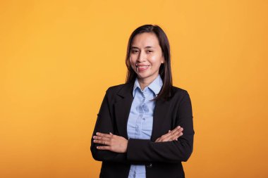 Filipinli resmi takım elbiseli bir kadının portresi. Stüdyoda sarı arka planda poz veriyor. Fotoshot sırasında el ele tutuşuyor. Neşeli bir ifadeyle kameraya bakarak gülümseyen genç bir yetişkin.
