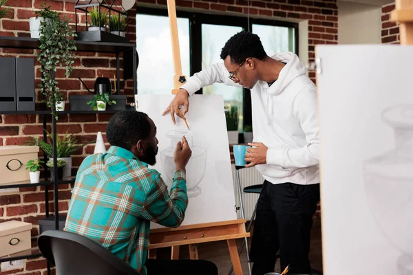 2人のアフリカ系アメリカ人男性の友人がアートクラスでキャンバスに絵を描き 一緒に芸術的な創造的な趣味を楽しみ 鉛筆で描くために自由な時間を過ごします 男性学生が一緒に作品を作る — ストック写真
