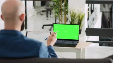 İşadamı şirket stratejisi planlamak için dizüstü bilgisayarını kullanarak ofisteki yeşil ekrana bakıyor. İzole edilmiş telif alanı görüntüsü üzerinde çalışan Ortadoğulu adam, birlikte çalışma alanında girişimcilik kavramı.