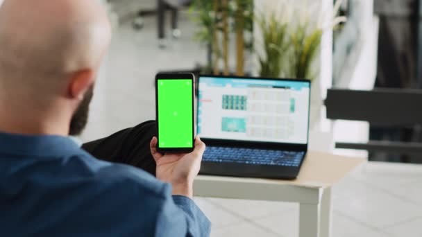 员工拿着装有绿屏的手机 而他却在看笔记本电脑运行的统计记分板 有独立陈列铬钥匙的商人 在公司工作 代理成功 — 图库视频影像