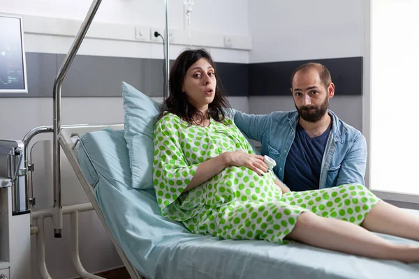 夫は避妊を妊娠中の女性を支援し 病棟で呼吸法を行います 診察中に医者が来て労働を開始するのを待ってベッドに寝そべって妊娠した患者 — ストック写真