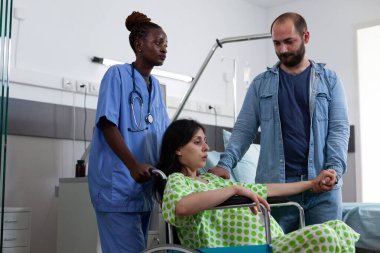 African american nurse taking pregnant woman in wheelchair to maternity room to delivery baby. Patient with pregnancy preparing for childbirth while being comforting by husband in hospital ward