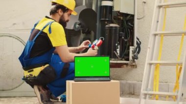 Seasoned mechanic employed by customer to find cause of faulty outdoor hvac system using measurement device, with nitrogen pressure loss over time displayed on chroma key laptop screen