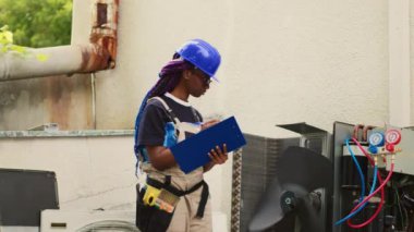 Proficient expert servicing outdoor air conditioner internal components, checking refrigerant level and calibrating thermostats. Capable specialist looking over maintenance plan on clipboard