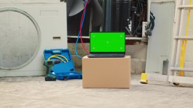 Green screen laptop in front of out of service outside air conditioner. Mock up chroma key gadget display next to damaged external HVAC system in need of expert maintenance
