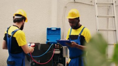 Expert technicians team working with manifold gauges to check air conditioner refrigerant levels, writing result on clipboard. Skillful mechanics using barometer benchmarking hvac system tool