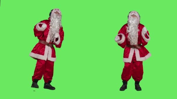 オーディオで楽しんでいる赤いスーツの男は 冬の季節の休日を祝うためにヘッドフォンで音楽を聞きます 白ひげダンスと緑色の背景に曲を楽しむサンタ — ストック動画