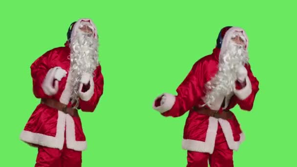 カメラで楽しむポジティブな季節のキャラクターは ヘッドフォンで緑色の背景を囲んで踊ります サンタクロースは スタジオで現代の曲を楽しんで幸せな人 クリスマスの休日 — ストック動画