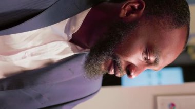 Dikey video, Afrikalı Amerikalı iş adamı, ofisteki günlük şirket dahili görevlerinin videosunu çekmek için akıllı telefonu selfie modunda kullanıyor. İş yerindeki çalışanın kendini iş görüşmelerini açıklarken görüntüsü.