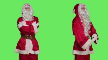 Beyaz sakallı, Noel Baba kostümü giymiş bir adam yeşil ekran arka planına karşı duruyor. Kış tatili ruhunu yaymaya hazır, Aralık mutluluğunu resmeden kişi..