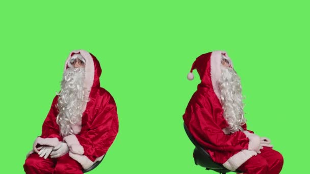 圣诞老人坐在孤立的绿屏背景上的椅子上 圣爪体现着红白相间的装束 欢天喜地的男人登广告庆祝节日 — 图库视频影像