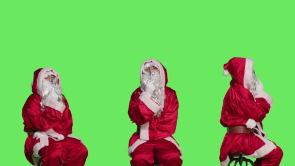 椅子のブレインストーミングのサンタは グリーンスクリーンの背景の上に座って クリスマスイブの休日の祝賀の前にプレゼントについて考える贈り物のアイデア スタジオで聖なるニックとして服を着た若い男 — ストック動画