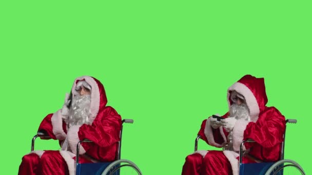 スマートフォンを使ったマンサンタクロース ビデオゲーム スタジオで電話で話す 障害のある車椅子で父クリスマスを描いた人 楽しいゲームやチャット — ストック動画