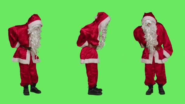 オールドサンタはスタジオで背中の痛みに苦しんでおり 完全な体の緑色の背景の上に立っている感じがします クリスマスイブ休暇中に傷ついた脊椎を扱う聖なるニックを描く男 — ストック動画