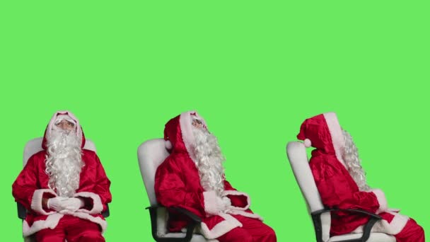 赤い衣装でクリスマスイブを祝う緑色の背景 陽気な人に対する椅子のサンタクロースのキャラクター 象徴的な冬のスーツが付いている12月の休日の若い大人の広告 — ストック動画