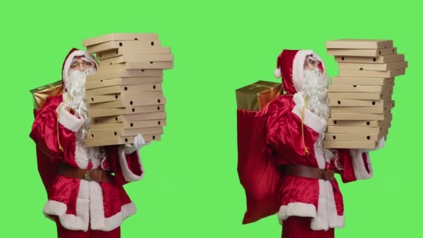 サンタは緑色の背景にピザ箱を配達し ファーストフードの大きな山を運び 子供のための玩具を持って袋を運びます お祝いの赤いコスチュームでセントニック スタジオの配達人のように演じる — ストック動画