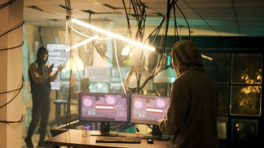 Diverse people applauding young hacker about cyberwarfare success, celebrating illegal activity achievement at night. Cyber criminals feeling happy about successfully stealing government data.