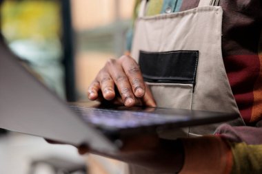 Depo çalışanı dizüstü bilgisayarı tutuyor sipariş detaylarını kontrol ediyor, depoda teslimat için ürünleri hazırlıyor. Afro-amerikan çalışanı mal kalite kontrolü yapıyor. Yakın çekim.