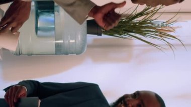 Dikey video Neşeli Afro-Amerikalı iş adamları gece vardiyası sırasında su deposu sohbetinin keyfini çıkarıyorlar. Neşeli işçi, iş arkadaşıyla konuşurken bir fincan kahve içip rahatlıyor.