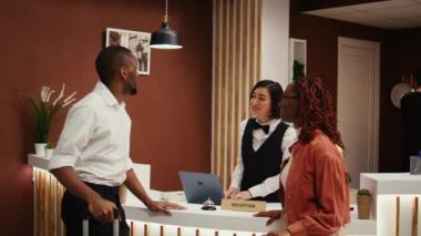 Asyalı resepsiyonist otel resepsiyonunda turistlere ekstra oda konforu satılıyor. Mutlu konuklar kontrol sırasında ek hizmetler ve kişisel deneyimler talep ediyor
