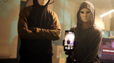 Team of masked hackers broadcasting live threat video, asking for passwords ransomware instead of leaking data. People with scary masks threatening to expose government information. Handheld shot. clipart