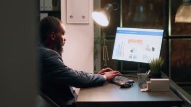 Tecrübeli bilgisayar operatörü gece vardiyası sırasında masa başında oturuyor, şirket muhasebe raporları ve modern ofisteki masalarda çalışıyor.