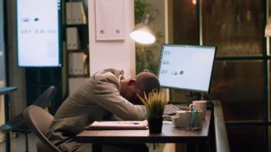 Çok çalışan Afrikalı Amerikalı iş adamı gece ofiste çalışırken masa başında uyuyor. Uykulu çalışanın gece vardiyasında tek başına uyuması ve yarım kalan işlerle uğraşması.