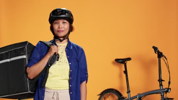 Portret Uśmiechniętego Azjatyckiego Motocyklisty Trzymającego Termalny Plecak Odizolowany Pomarańczowym Tle — Wideo stockowe