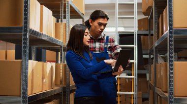 Young man and woman checking inventory on laptop, doing quality control for order distribution and supply chain management. Team of people using laptop to work on logistics in storage room.