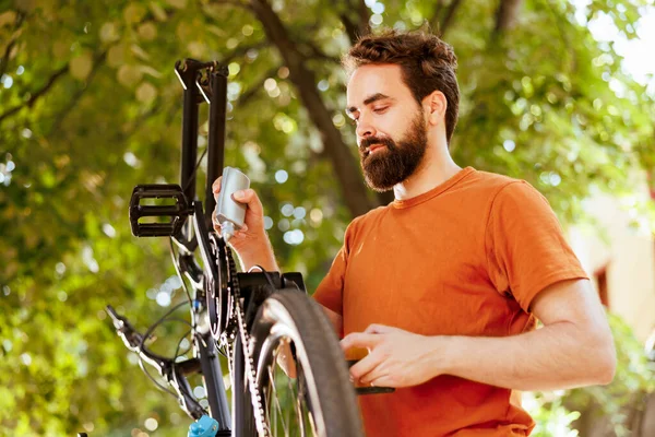 自転車チェーンをグリースするために専門の潤滑油を使用するスポーティ専用男性 画像は シームレスなサイクリング体験のための彼の自転車チェーンリングを熟練した慎重な男を表示します — ストック写真