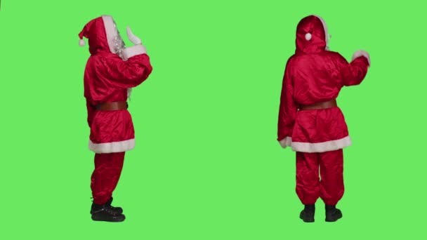 喜庆的圣徒尼克向站在全身绿叶之上的人们致意 穿着节日的红色西服来传播节日的精神 男人挥手打招呼 准备庆祝圣诞节 — 图库视频影像