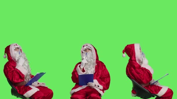 クリップボード紙を使用してメモを取る聖人のニックキャラクターは お祝いの赤い衣装で椅子に座っています サンタクロースを描き 子供に関する情報を書く大人のコンセプト — ストック動画