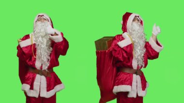 Noel Baba, yeşil perde arkaplanı üzerinden olumlu bir şeyler vermek ve anlaşmanın sembolünü vermek için kamerada baş parmağını gösteriyor. Takım elbiseli Noel Baba hediye çantasıyla onaylıyor..
