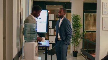 Mutlu Afro-Amerikan iş arkadaşları gece vardiyasında su deposu tartışmasının keyfini çıkarıyorlar. Ofisteki meslektaşımla konuşurken gülümseyen bir çalışanın kahve içmesi rahatlatıcı.