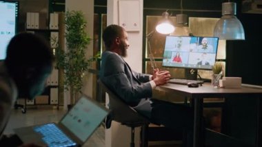 Ofisteki Afrikalı Amerikalı çalışanlar evden iş arkadaşlarıyla telekonferans toplantısı yapıyor. İşadamı, gece vardiyası sırasında şirket personeliyle sohbet ediyor.