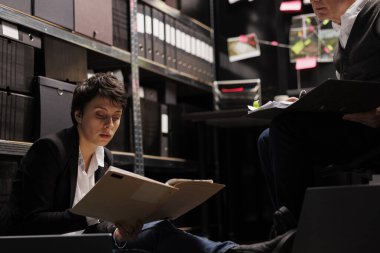 Suç mahalli kanıtlarıyla dolu dosyaları tutan yorgun müfettiş arhiv odasında kriminoloji raporunu analiz ediyor. Kayıp şahıs davasında fazla mesai yapan özel dedektifler.