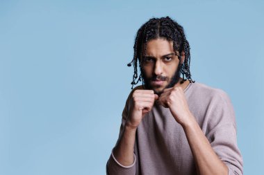 Güçlü Arap dövüşçü yumruklarını sıkmış ve kameraya bakarak boks pozisyonunda duruyor. Kendine güveni olan biri ciddi bir yüz ifadesi portresiyle dövüş pozu veriyor.