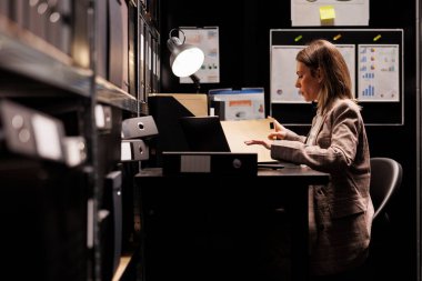 Şirket depolarını düzenleyen, muhasebe raporlarını analiz eden, idari kayıtları kontrol eden bir yönetici. İş kadını muhasebe belgeleri okuyor, gece geç saatlere kadar depoda çalışıyor.