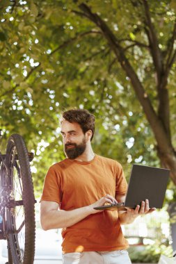 Görüntü teknolojisi, genç adama bisiklet ekipmanlarının bakımında ve korunmasında yardımcı oluyor. Ev bahçesinde bisiklet tamir eden laptoplu, spor düşkünü, beyaz bir erkek..