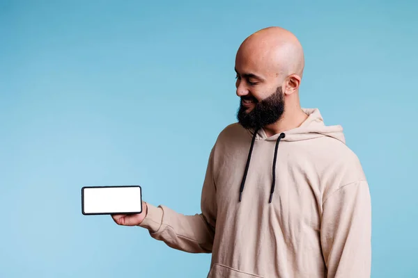 携帯電話を持っているアラブの男は コピースペースで空白の画面を見ています 広告のための水平モードの空白のタッチスクリーンが付いているスマートフォンを示す陽気な注意のない人 — ストック写真