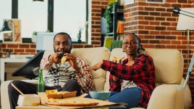 Young couple eating slices of pizza and watching show on television, laughing and being together. Man an woman in relationship enjoying takeaway meal to watch favorite film on tv. Tripod shot.