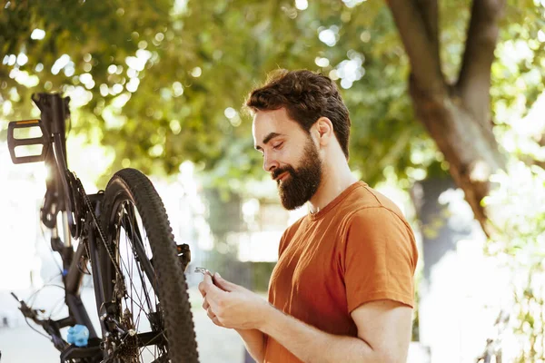 スポーティな白人男性は 毎年夏のメンテナンスとして外で自転車を提供しています 現代の自転車の屋外を維持し 修理する専門用具と働く運動の男性の自転車 — ストック写真